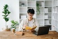 Handsome and talented young Asian man student working on his project assignment, using laptop and tablet to search an online Royalty Free Stock Photo