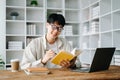 Handsome and talented young Asian man student working on his project assignment, using laptop and tablet to search an online Royalty Free Stock Photo
