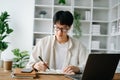 Handsome and talented young Asian man student working on his project assignment, using laptop and tablet to search an online Royalty Free Stock Photo