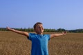 A handsome tanned child boy stands in a wheat field with his arms outstretched to the sides and enjoys summer freedom. A
