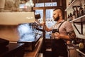 Tattooed barista with stylish beard and hairstyle working on a coffee machine in a coffee shop or restaurant