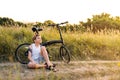 A handsome boy sits on the road near the bike. The boy is resting while cycling at sunset. Royalty Free Stock Photo