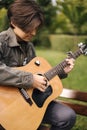 Handsome teenage playing acoustic guitar with capo. Boy sitting on bench and playing music