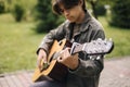 Handsome teenage playing acoustic guitar with capo. Boy sitting on bench and playing music