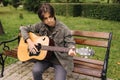 Handsome teenage playing acoustic guitar outdoor in Autumn time. Boy sitting on bench and playing music