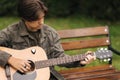 Handsome teenage playing acoustic guitar outdoor in Autumn time. Boy sitting on bench and playing music