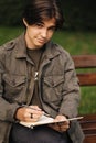 Handsome teenager painting something in his notepad outdood during the break. Talanted young boy Royalty Free Stock Photo