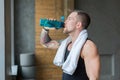 Handsome thirsty young man in gym, drinking water from bottle