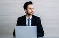 Handsome thoughtful bearded sitting at his desk while using laptop computer and looking away in modern office. People and