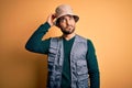 Handsome tourist man with beard on vacation wearing explorer hat over yellow background confuse and wondering about question