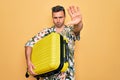 Handsome tourist man with blue eyes on vacation holding suitcase over yellow background with open hand doing stop sign with Royalty Free Stock Photo