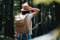 Handsome traveler woman with backpack and hat standing in forest. Young hipster girl walking among trees on sunset Royalty Free Stock Photo