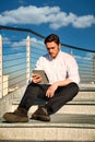 Handsome trendy man wearing white shirt sitting outdoor on metal stairs step Royalty Free Stock Photo