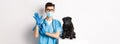 Handsome vet doctor in veterinarian clinic put on gloves and medical mask, examining cute little dog pug, white Royalty Free Stock Photo