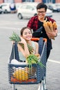 Handsome vietnamese man holds paper bags with food pushing in front of him shopping trolley with his happy beautiful Royalty Free Stock Photo