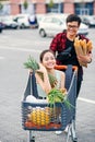 Handsome vietnamese man holds paper bags with food pushing in front of him shopping trolley with his happy beautiful Royalty Free Stock Photo