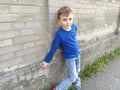 A handsome white boy in a blue sweater or longsleeve is standing against the wall and smiling. Child on a brick wall background.