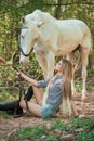 Handsome woman sitting on the ground with brown horse near her. Royalty Free Stock Photo