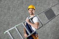 Handsome working man in hard hat holding ladder against color