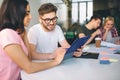 Handsome yougn man look at plastic tablet brunette hold in hands. They sit together. Another couple works behnid them Royalty Free Stock Photo