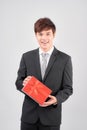 Handsome yound man in suit is posing on white background with red gift box in hands, looking at camera and smiling Royalty Free Stock Photo