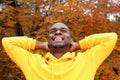 Handsome young african american man against autumn leaves in background smiling with hands behind head Royalty Free Stock Photo