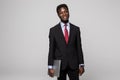 Handsome young African man carrying laptop and looking at camera while standing against grey background Royalty Free Stock Photo