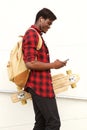 Handsome young african man with skateboard and back pack looking at cell phone Royalty Free Stock Photo