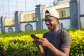 handsome young african man smiling and using his phone, browsing the internet, surfing the web