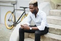 Handsome young Afro American man in casual wear is using smartphone while sitting on stairs outdoors Royalty Free Stock Photo