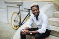 Handsome young Afro American man in casual wear is using smartphone while sitting on stairs outdoors Royalty Free Stock Photo