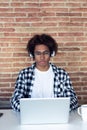 Handsome young afro-american man with eyeglasses listening to music with headphones while using his laptop at home Royalty Free Stock Photo