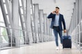 Handsome young arab businessman talking on cellphone and carrying suitcase in airport Royalty Free Stock Photo