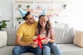 Handsome young Arab guy covering his girlfriends eyes, making birthday surprise, giving her wrapped gift at home Royalty Free Stock Photo