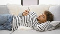 Handsome young arab man, with a serious expression, deep into online texting, lying relaxed on his living room sofa at home, using Royalty Free Stock Photo