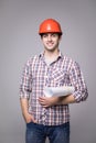 Handsome young architect in suit and protective helmet, looking at camera and smiling, on gray background Royalty Free Stock Photo