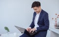 Handsome young Asian businessman wearing formal clothes or suit, smiling in happiness, confidence, success, sitting at desk and Royalty Free Stock Photo