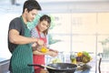 Handsome young Asian husband is beating fresh organic eggs to cooking healthy food while beautiful wife helping beside in modern Royalty Free Stock Photo