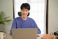 Handsome young Asian male college student in cozy sweater using laptop, at home Royalty Free Stock Photo