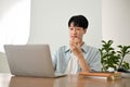 Handsome young Asian male college student eating donut while working on his project on laptop Royalty Free Stock Photo