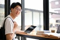 Handsome young Asian male college student wearing glasses sits at a table in a coffee shop Royalty Free Stock Photo