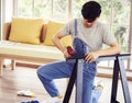 Young Asian man assembling furniture in new apartment and tightening screw with electric screwdriver