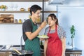 Handsome young Asian man with casual clothes is smiling, feeding to beautiful woman while blowing food, showing funny face, and Royalty Free Stock Photo