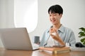 Handsome young Asian man eating donut and sipping coffee while working on his project on laptop Royalty Free Stock Photo