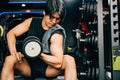 handsome young Asian man sitting on an exercise bench holding a heavy dumbbell Royalty Free Stock Photo