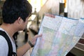 Handsome young Asian tourist exploring map for right direction at the train station. Travel and tourism concept. Selective focus a