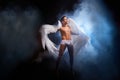 Handsome young athletic man with a bare torso who looks like an angel with white wings. Model dancer posing in a dark Royalty Free Stock Photo
