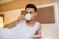 Handsome young awake man drinking cup of coffee in the white bed Royalty Free Stock Photo