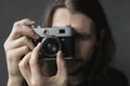 Handsome young bearded man with a long hair and in a black shirt holding vintage old-fashioned film camera on a black Royalty Free Stock Photo