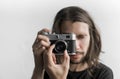 Handsome young bearded man with a long hair and in a black shirt holding vintage old-fashioned film camera on a white Royalty Free Stock Photo